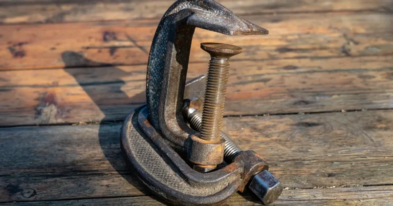 Rusty bar clamp resting on a wooden workbench, ready for a glue cleanup