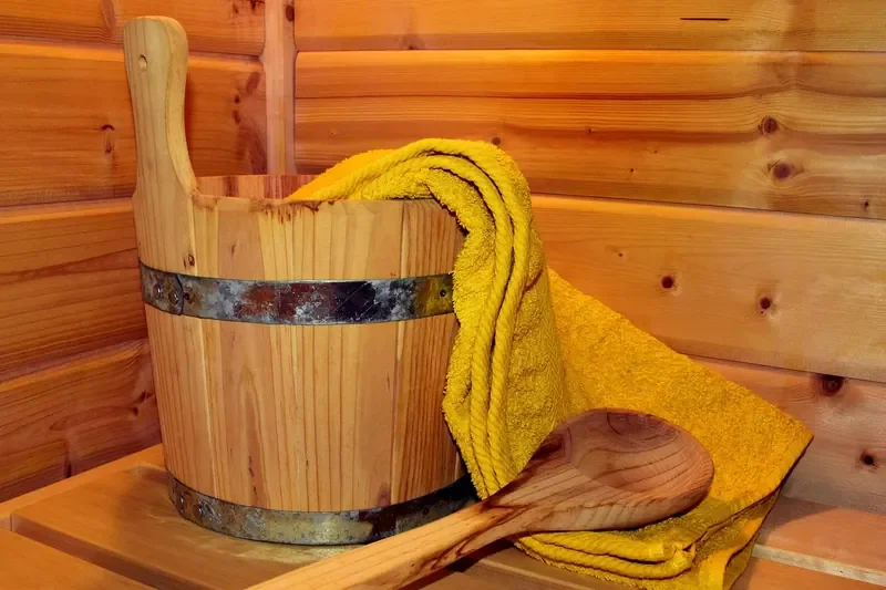 Wooden sauna bucket, ladle and towel against a wood-paneled sauna wall Wooden sauna bucket, ladle and towel against a wood-paneled sauna wall