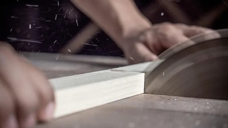 Close-up of a board being guided through a table saw blade during a wood cut