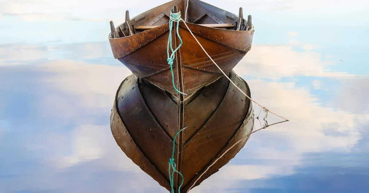 Varnished wooden rowboat floating on calm water