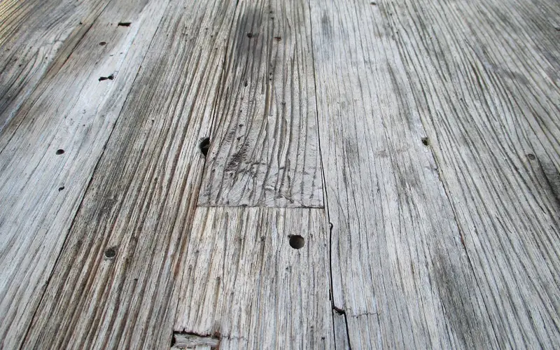 Weathered gray deck boards with old fastener holes and a split along one board