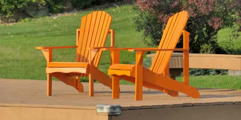 two orange-painted Adirondack chairs on a wood deck overlooking a lawn