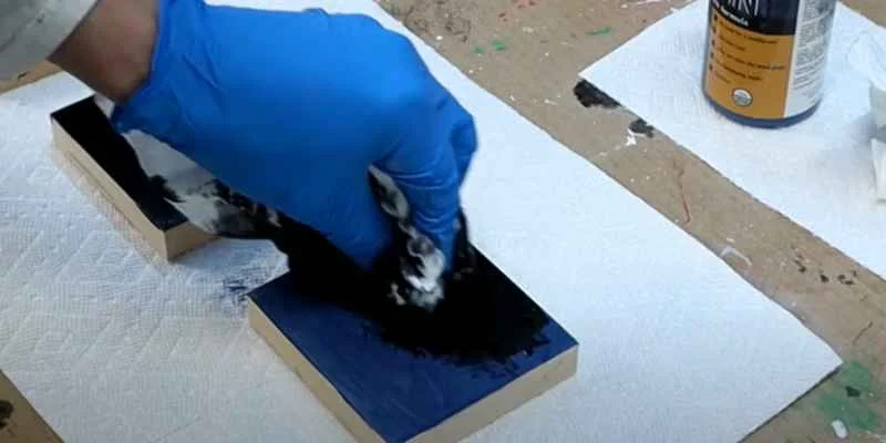 gloved hand wiping black stain onto small wood blocks gloved hand wiping black stain onto small wood blocks