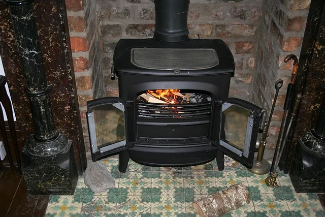 Wood burning stove with a blower fan, glass doors open showing an active wood fire