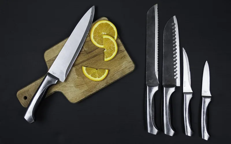 kitchen knife resting on a small wood cutting board next to a full knife set, showing blade edges