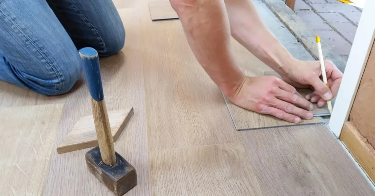 Hands positioning a wood floor plank next to a mallet during flooring work