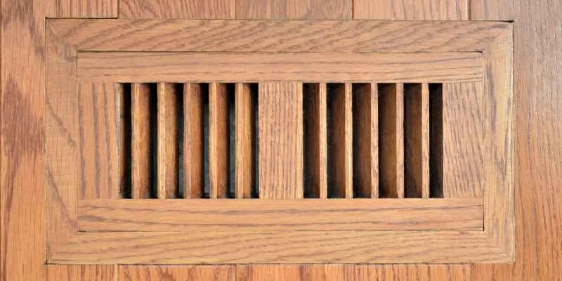 Wood floor vent register with slatted grille flush-mounted in hardwood flooring