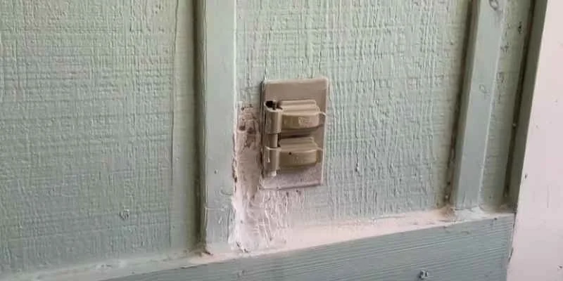 Exterior wood siding around an electrical outlet showing cracked paint and rot damage before treatment