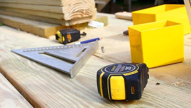 Tape measure and speed square laid on stacked lumber for measuring length and width