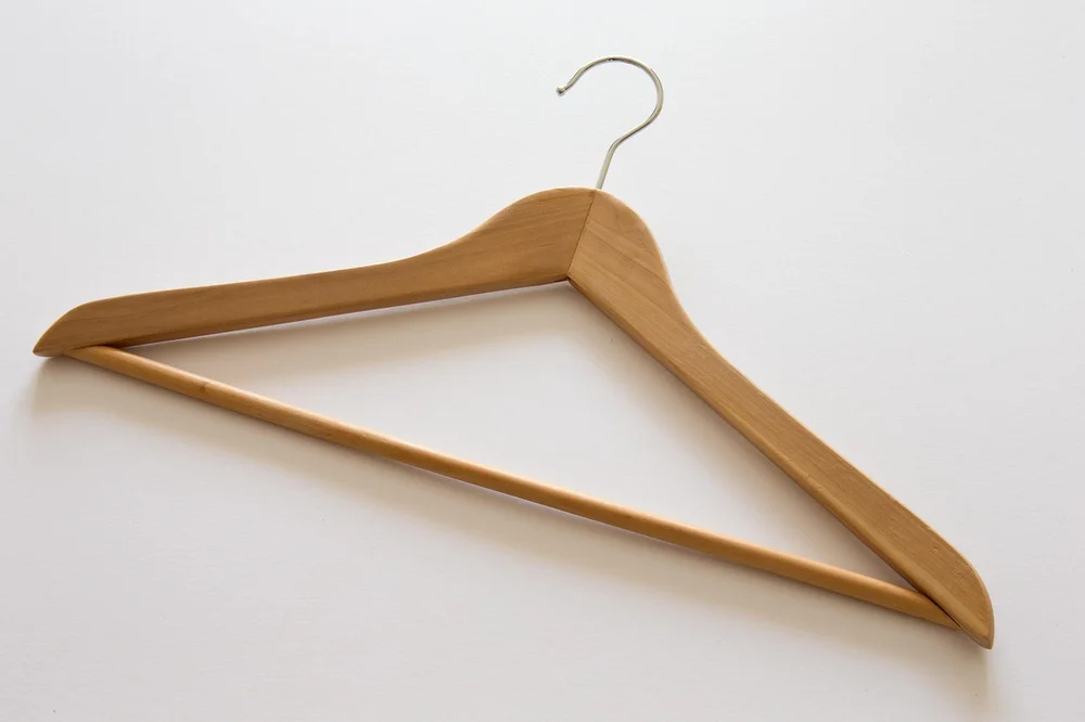 Close-up of a solid wood coat hanger showing the contoured shoulder shape and swivel hook Close-up of a solid wood coat hanger showing the contoured shoulder shape and swivel hook