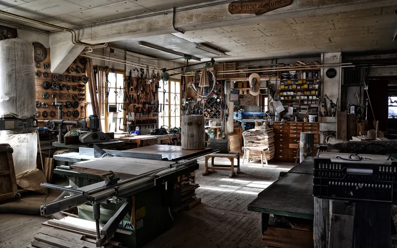 woodworking shop with table saw, hand tools on a pegboard wall, and stacked lumber