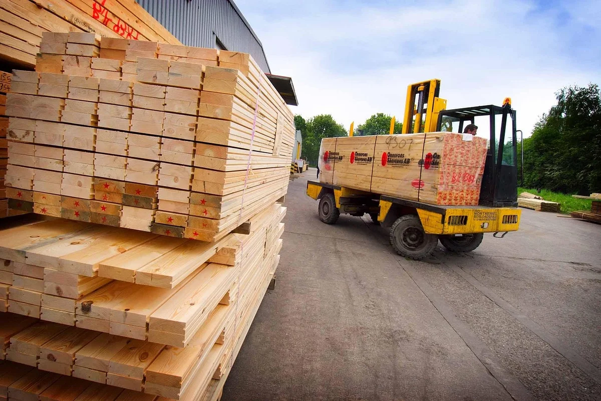 Forklift loading stacked lumber sheets at a building supply yard