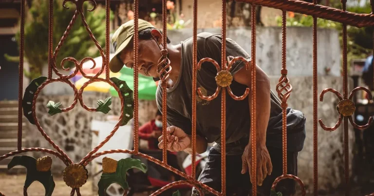 worker applying metallic paint and primer coating to an ornate wrought iron gate
