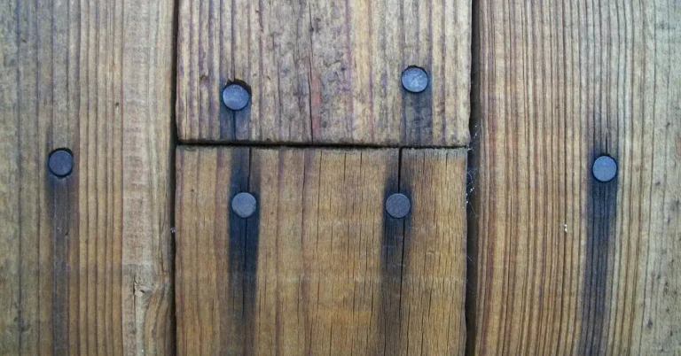 Rusty nail heads bleeding dark stains down weathered wood plank grain