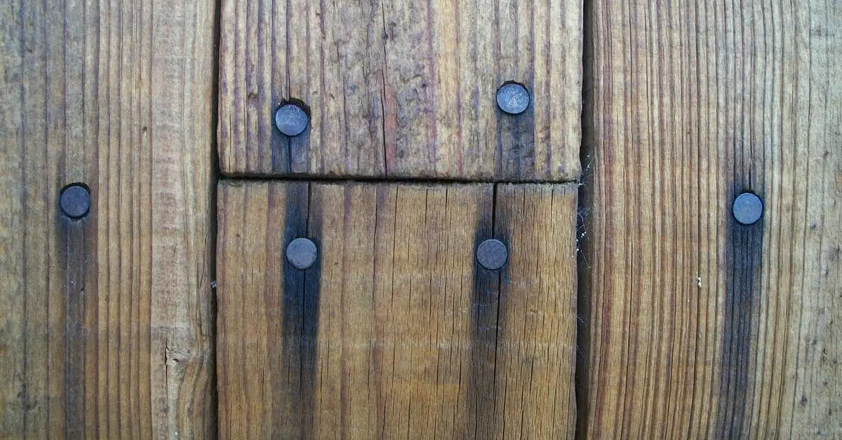 Rusty nail heads bleeding dark stains down weathered wood plank grain