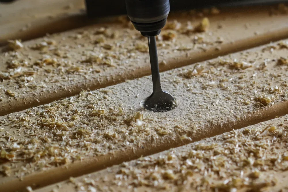 Drill bit boring a hole into a wood board surrounded by shavings