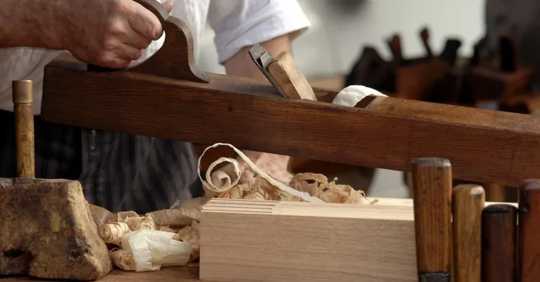 carpenter using a wooden jointer plane, curled wood shavings piling up on the bench