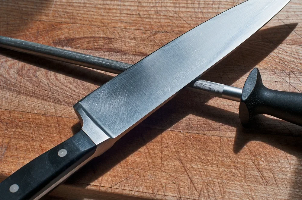 Chef knife and honing steel resting on a hardwood cutting board
