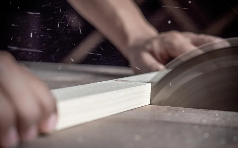 Carpenter's hands guiding a saw through a wood board for a door frame jamb