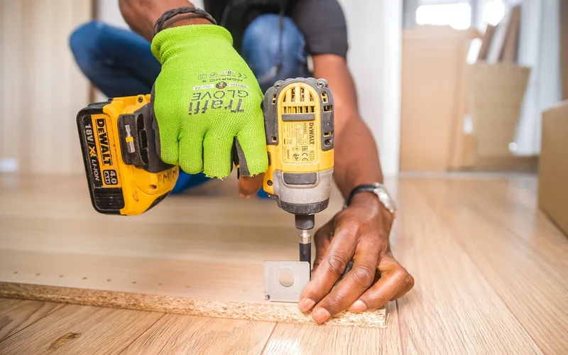 driving a hanger bolt through a metal mounting plate into a table leg with a power drill