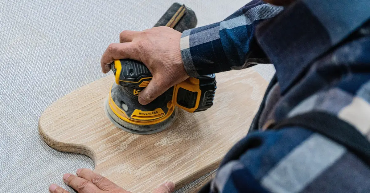 Orbital sander smoothing a wood surface with 220-grit sandpaper to remove carbon paper stains