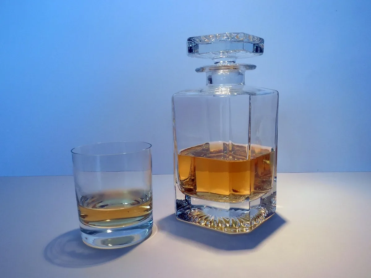 Square glass decanter and a tumbler of whiskey on a plain surface