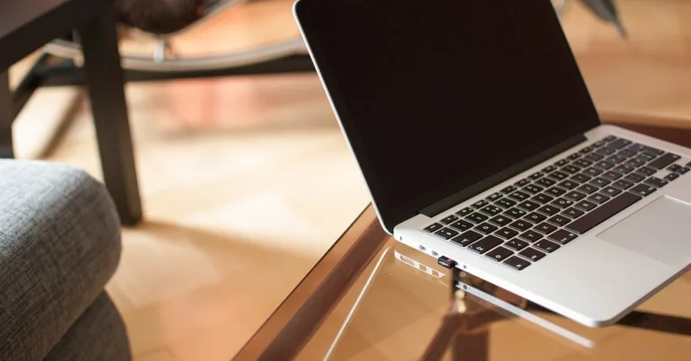 Laptop resting on a glass-top table showing the glass surface meeting a dark table frame