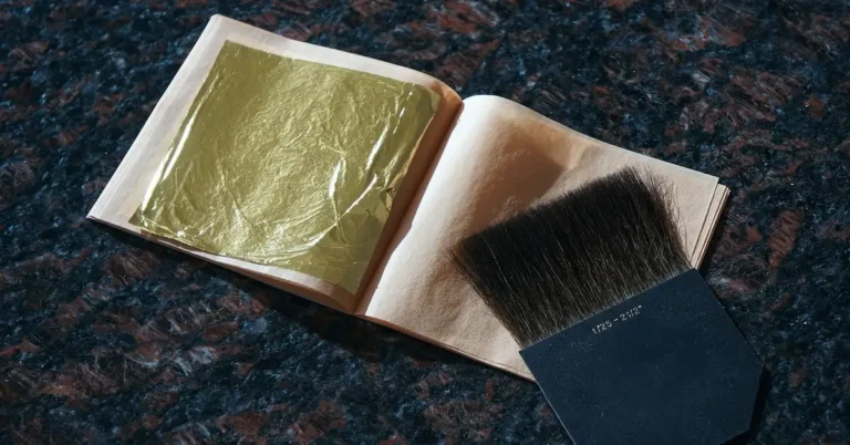 Gold leaf sheet in a booklet next to a flat gilding brush