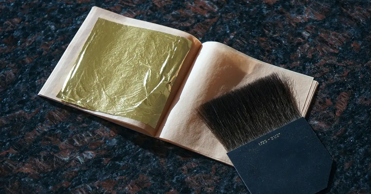 Gold leaf sheet in a booklet next to a flat gilding brush