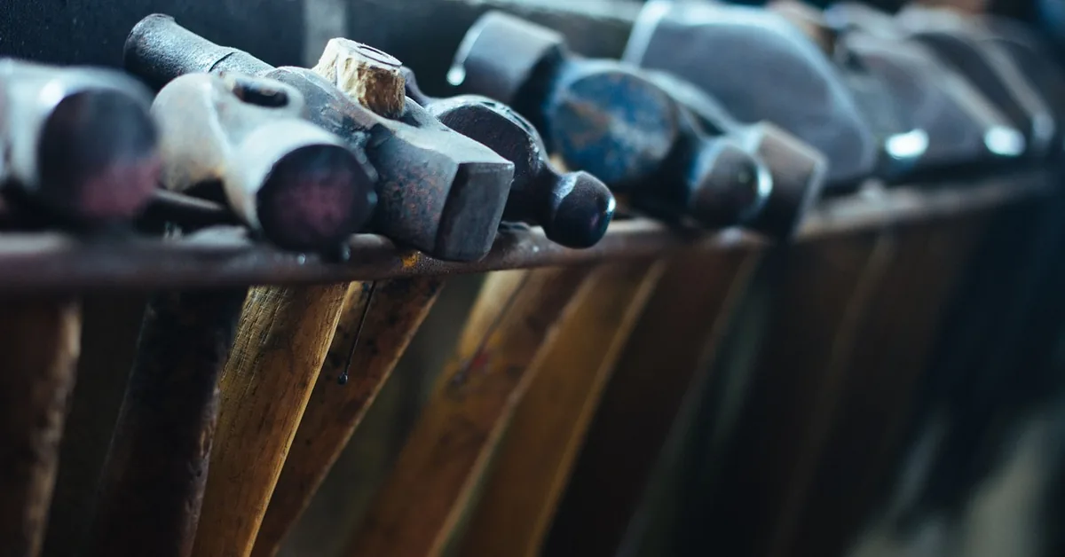 row of hammers with wooden handles hanging on a workshop tool rack