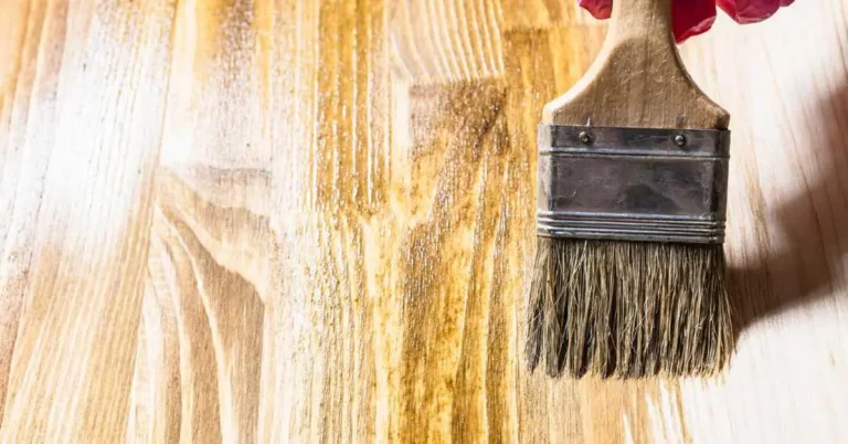 Gloved hand brushing oil-based wood stain onto a raw pine board