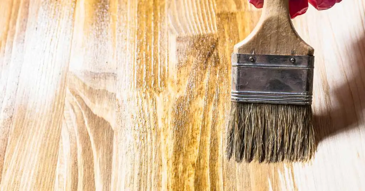 Gloved hand brushing oil-based wood stain onto a raw pine board
