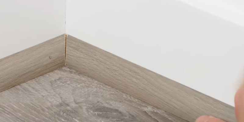 Mitered quarter round corner joint against baseboard and dark painted wall