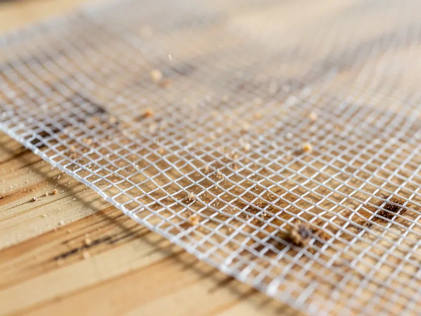 Open-mesh sanding sheet on pine wood with resin dust falling through the mesh instead of clogging the abrasive
