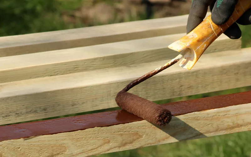 Roller applying paint to a bare wood surface outdoors