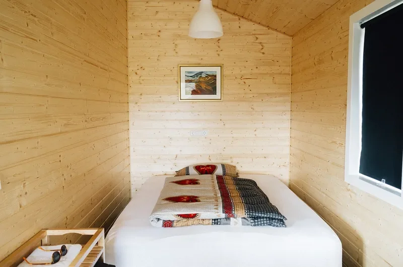 Pale wood paneled cabin bedroom with a simple platform bed