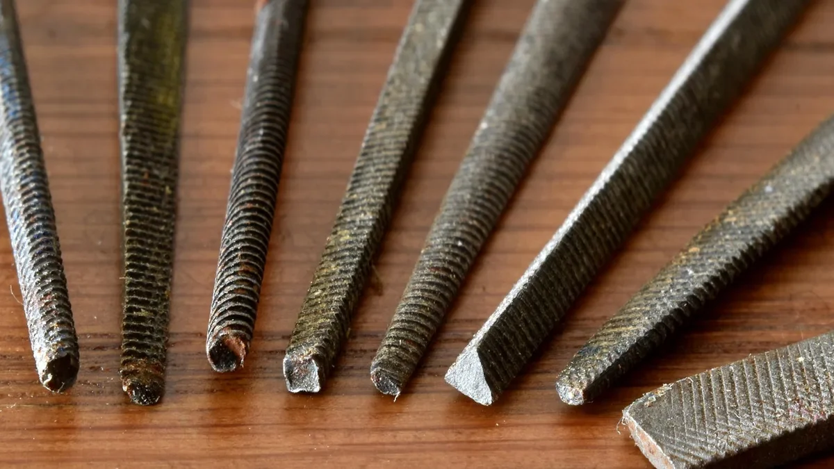 Set of steel rasps and files laid out on a wooden bench for shaping plywood