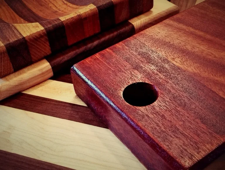 Red hardwood cutting board with a hand hole beside striped maple and dark wood boards