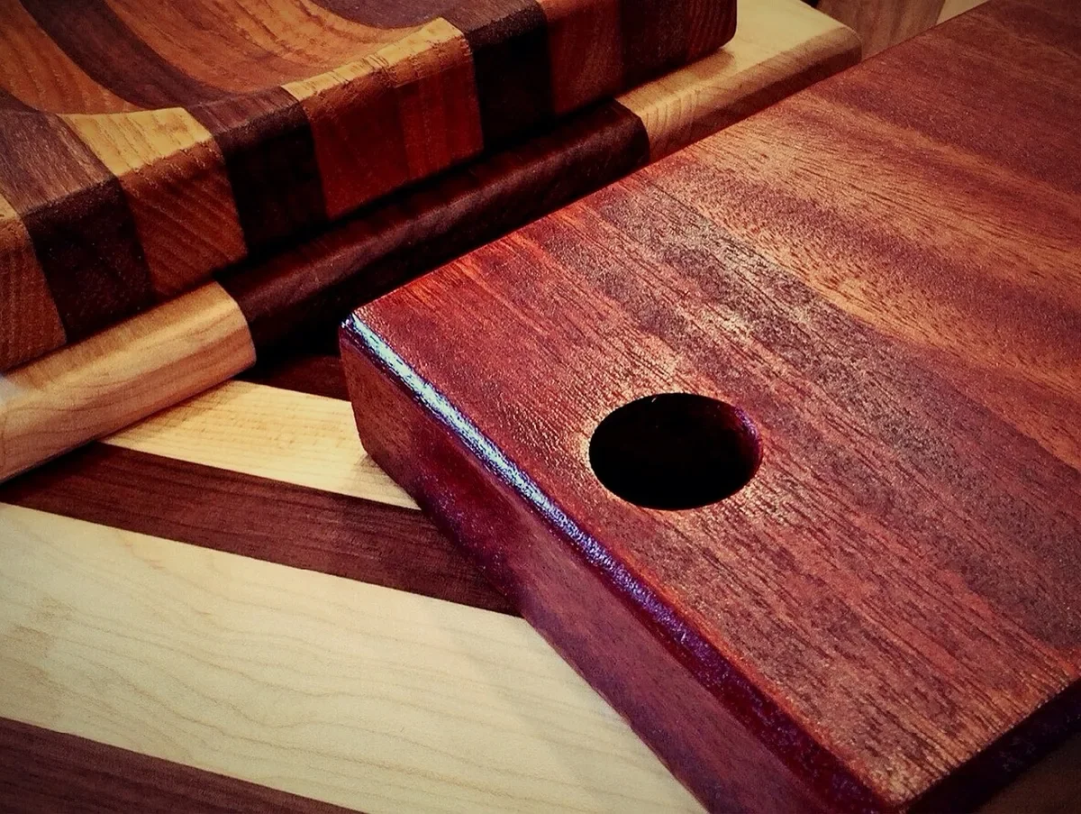 Red hardwood cutting board with a hand hole beside striped maple and dark wood boards