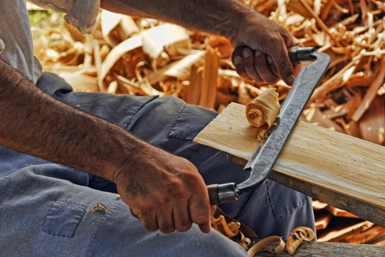 Hand tool shaping a wood board, shavings visible