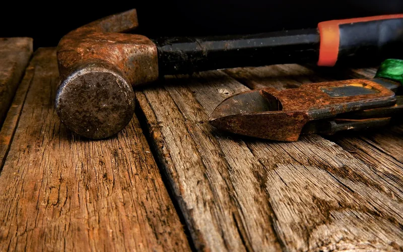 Surface rust on a hammer head and pruner blade resting on weathered boards