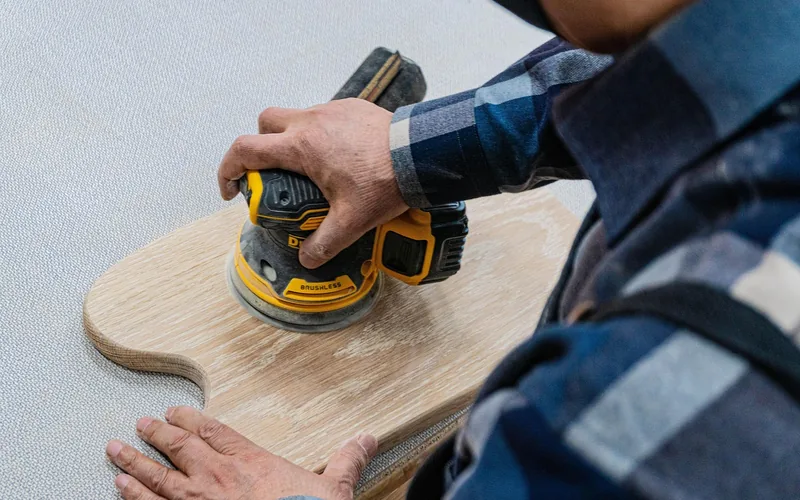 carpenter using an orbital sander to smooth a splintered wood surface before refinishing