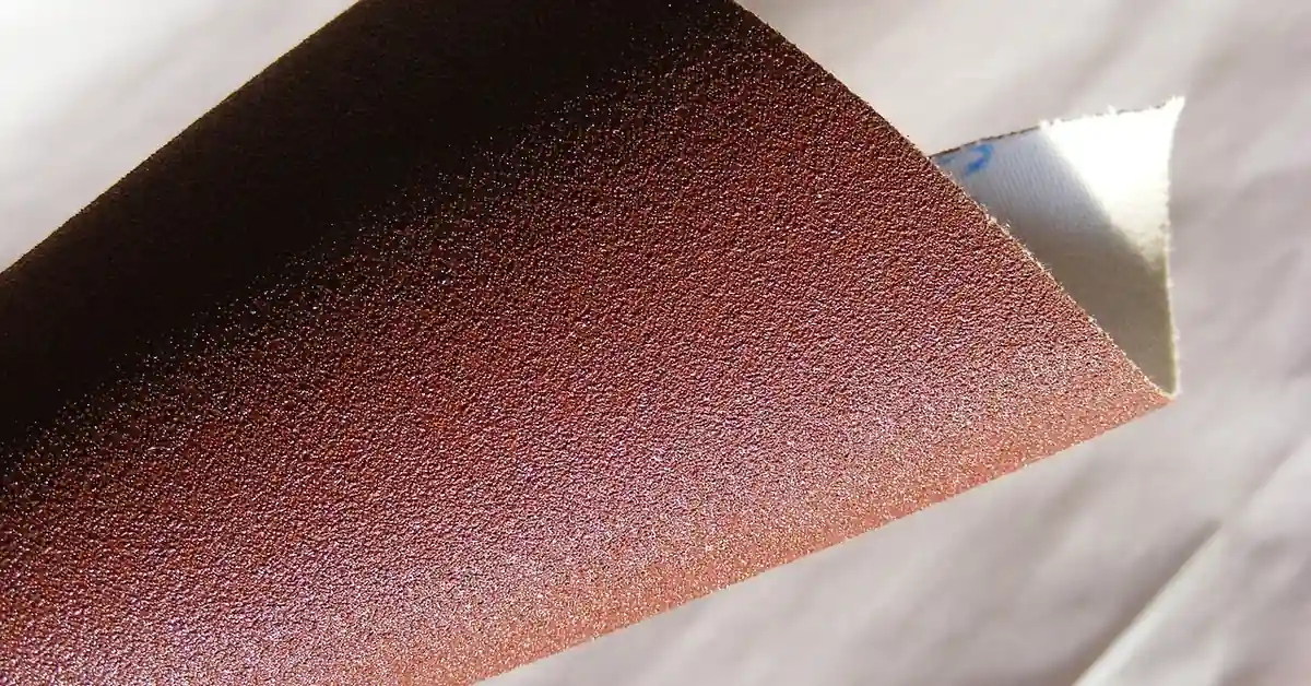 Close-up of fine-grit sandpaper sheet, the abrasive compared to 0000 steel wool