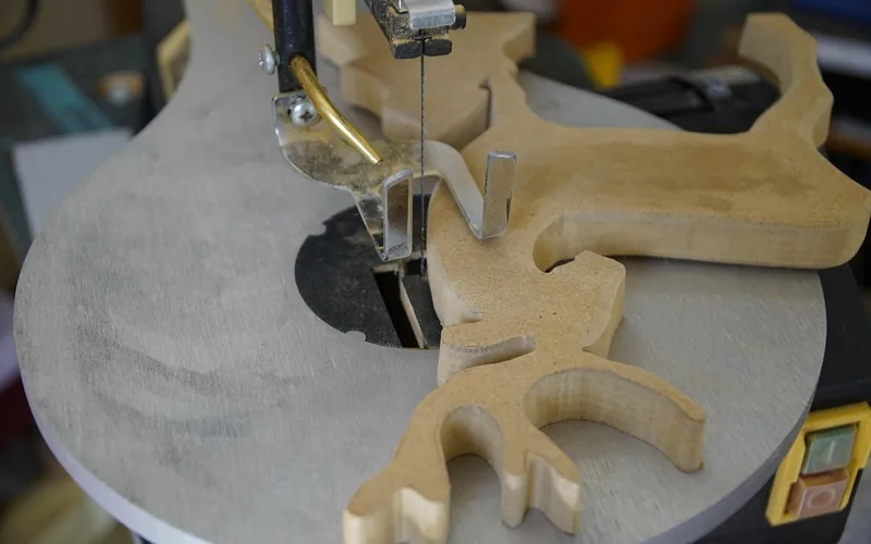 Narrow continuous blade cutting an intricate curved shape out of MDF on a scroll saw table Narrow continuous blade cutting an intricate curved shape out of MDF on a scroll saw table