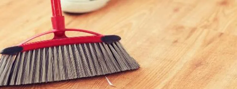 Angled broom sweeping loose dust and debris off a wood floor before mopping