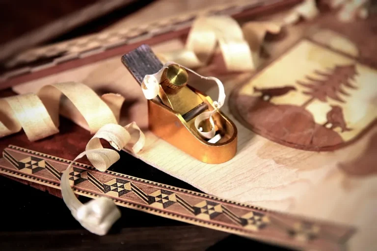 Small brass hand plane and pale shavings on thin wood veneer with marquetry inlay