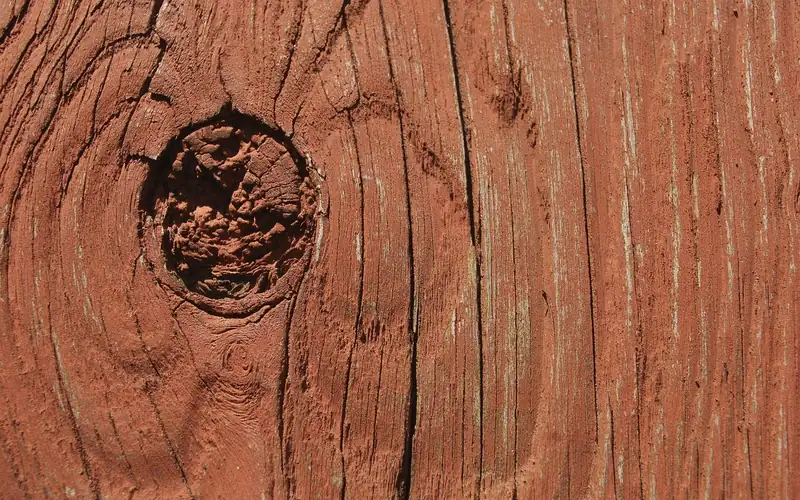 close-up of weathered wood board with knot hole and surface cracking that leads to splinters