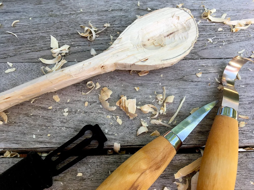 Two carving knives and fresh wood shavings on a workbench