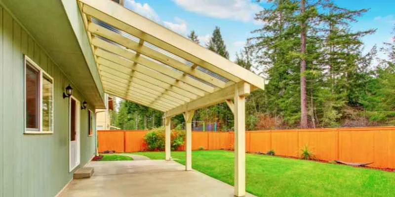 Wood patio cover with open beam roof structure attached to a house, overlooking a backyard