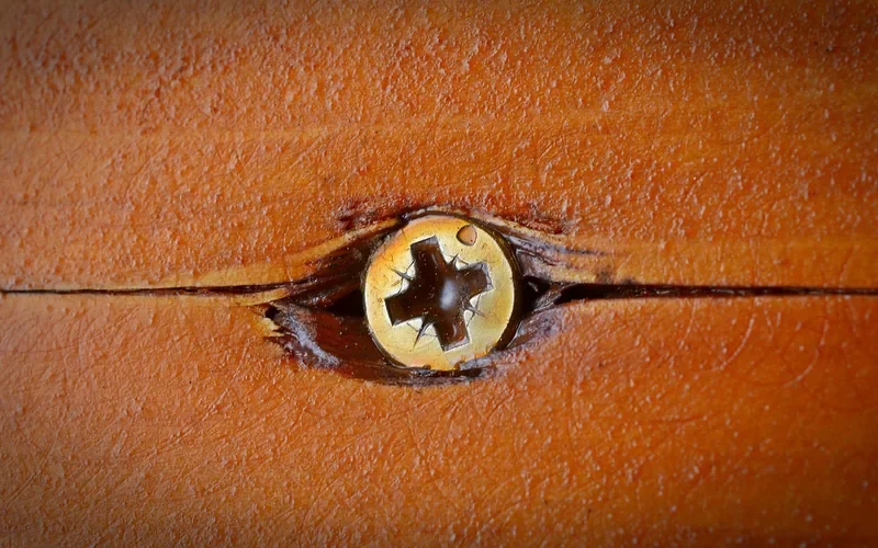 Screw head sitting in a split seam of an orange-stained wooden board